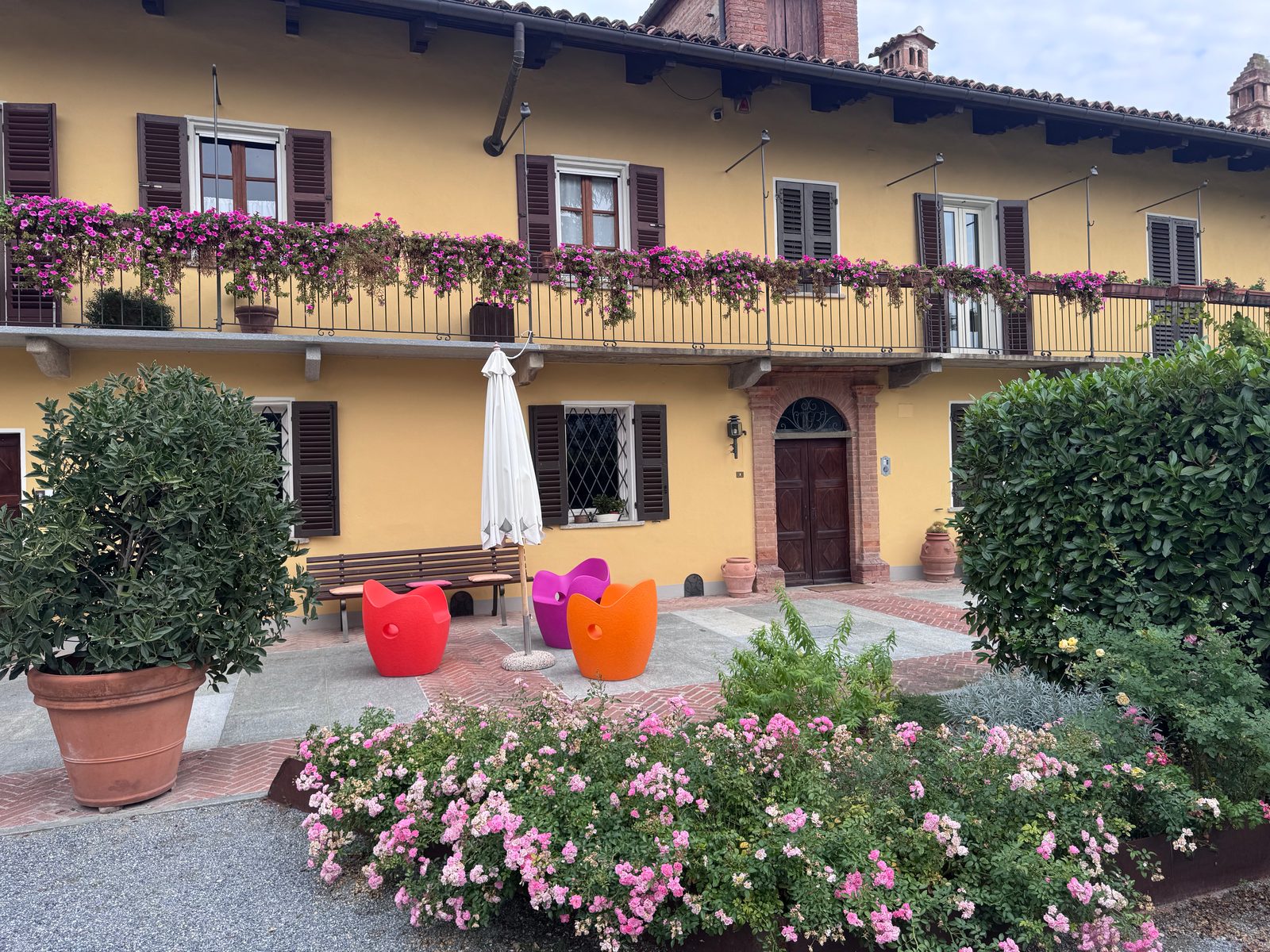 The yellow house at Oddero, with flowers along the balcony, colored chairs and roses in the courtyard