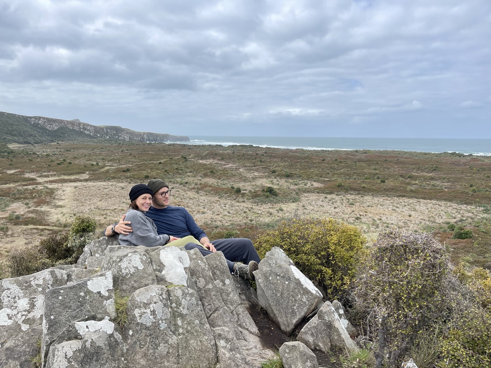 Thomas and Teri sitting together on a rocky outcrop above the dunes and the sea at Victory Beach